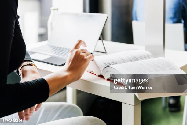 university student looking through large textbook while working - college books stock-fotos und bilder