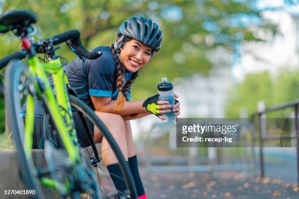 portrait of female biker smiling for camera in public park - bicycling imagens e fotografias de stock