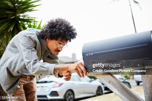 junger mann steht draußen und überprüft seinen briefkasten - briefkasten stock-fotos und bilder