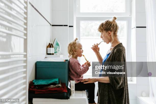 junge mutter mit einem kind, das morgens zähneknirschend putzt - daughter stock-fotos und bilder
