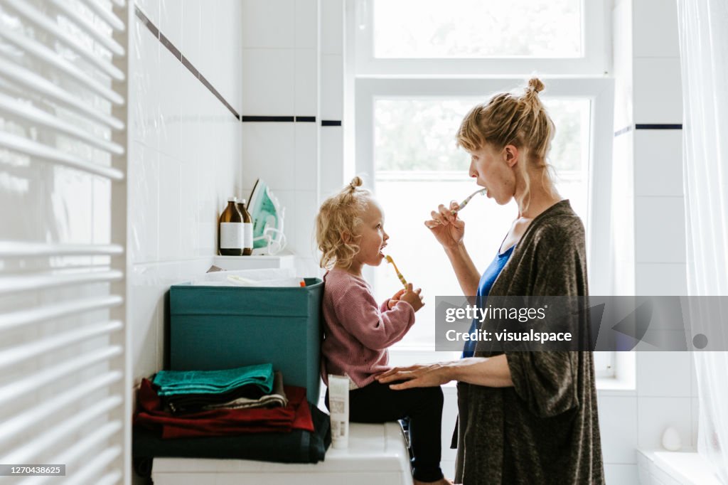 Young mother with a child brushing teeth in the morning