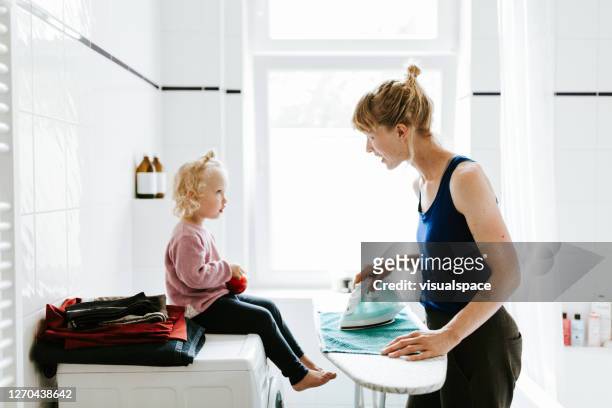 junge mutter mit einem kind, das handtücher im badezimmer bügelt - bügeln stock-fotos und bilder