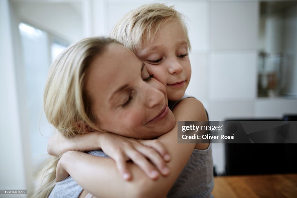 Affectionate mother and son with closed eyes hugging at home