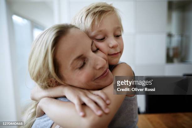 affectionate mother and son with closed eyes hugging at home - offspring stock-fotos und bilder