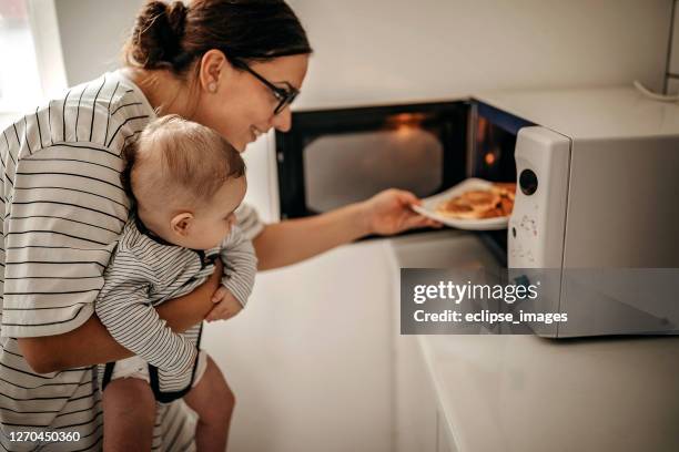 mutter bereitet essen mit baby in den armen - mikrowelle stock-fotos und bilder