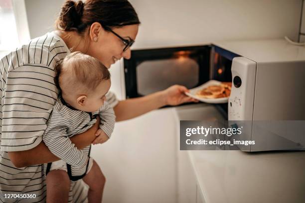 mother preparing food with baby in arms - microwave cooking stock pictures, royalty-free photos & images