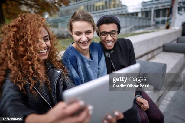 three happy friends looking at digital tablet together - girl 18 stock pictures, royalty-free photos & images