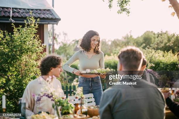 smiling female with cutting board serving food to friends at garden party - cutting board stock pictures, royalty-free photos & images