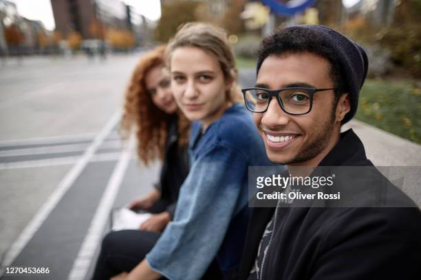 portrait of three smiling friends sitting together outdoors - 19 years stock pictures, royalty-free photos & images