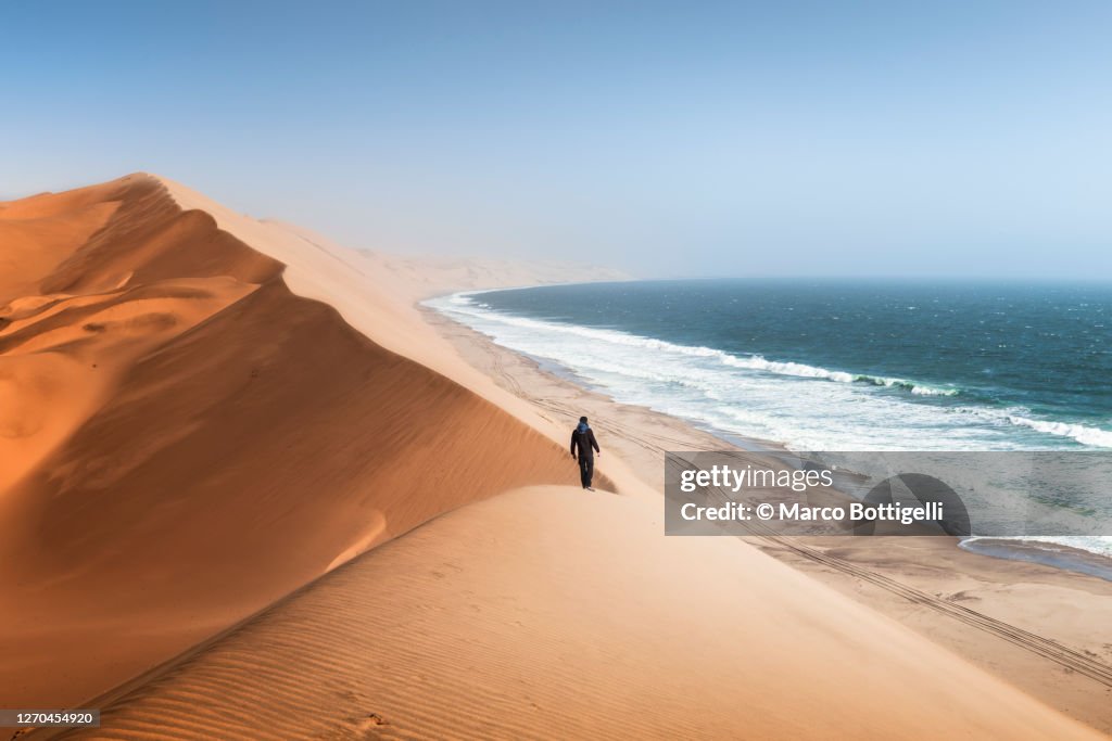 Man walking on sand dunes above the ocean, Namibia