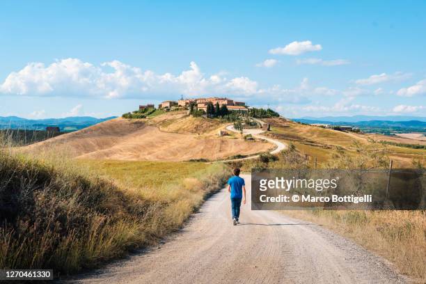 man walking on a gravel road to a rural village, tuscany - village foto e immagini stock