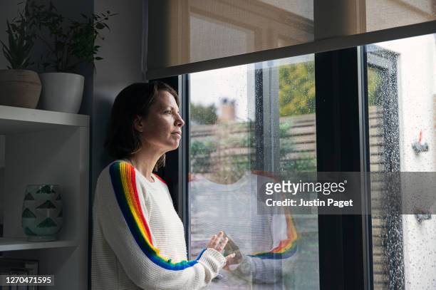 woman looking through window hopefully - quarantäne stock-fotos und bilder