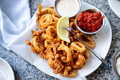 A Delicious Plate Of Deep Fried Calamari, Squid Fried To Perfection Cajun Style, Served With A Side Of Freshly Made Garlic Aioli Sauce And Cocktail Sauce, Fresh Lemon Wedges On The Side