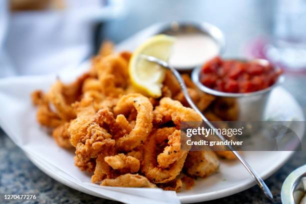 un delicioso plato de calamares fritos profundos, calamar frito al estilo cajún a la perfección, servido con una guarnición de salsa de aioli de ajo recién hecha y salsa de cóctel, cuñas de limón fresca en el lado - freír mediante inmersión total en aceite caliente fotografías e imágenes de stock