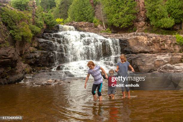 three kids walking in river beneath waterfall - minnesota river stock pictures, royalty-free photos & images