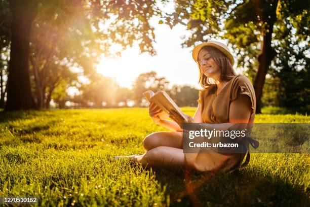 lectura en el prado al atardecer - mujer leyendo libro en el parque fotografías e imágenes de stock