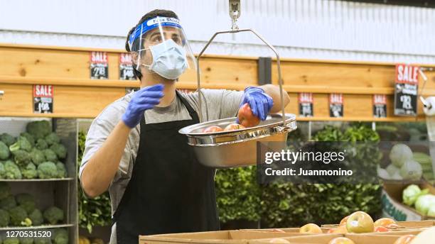 greengrocers shop employee putting apples in a scale wearing a protective face mask, a face shield and protective gloves - supermarket mask stock pictures, royalty-free photos & images