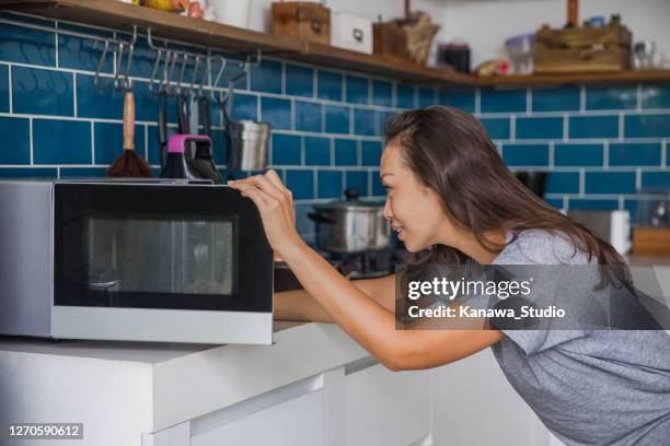 beautiful asian woman reheating her meals inside microwave. - microwave stock pictures, royalty-free photos & images