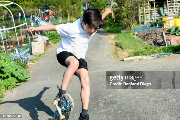 boy with brown hair wearing t[shirt and shorts performing skateboard trick. - skater boy hair stock pictures, royalty-free photos & images