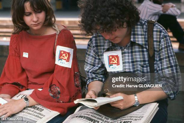 Jeune femme et jeune homme lisant le journal 'l'UNITA, avec des stickers collés à leur poitrine appelant à voter pour le Parti Communiste italien ,...