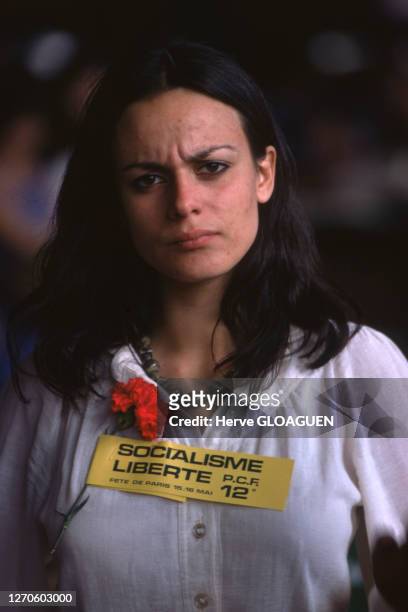Portrait d'une jeune femme avec une rose rouge accrochée à son chemisier et un autocollant "Socialisme liberté PCF" lors de la "Fête de Paris"...