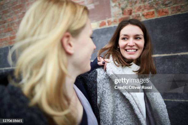 two smiling young women passing a wall outdoors - 經過 個照片及圖片檔