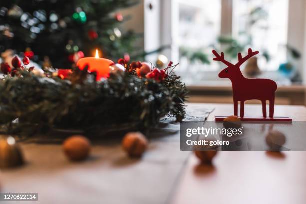 candel of advent wreath burning in front of festive christmas tree - advent wreath stock pictures, royalty-free photos & images