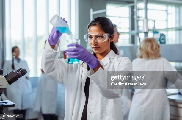 female university student pouring solution into beaker - purple glove stock pictures, royalty-free photos & images