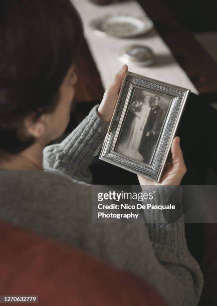 senior woman looking at a wedding photo of her parents - kin in de hand stock pictures, royalty-free photos & images