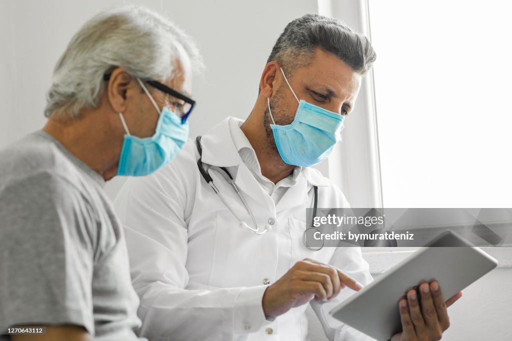 Doctor using digital tablet and talking to patient at home