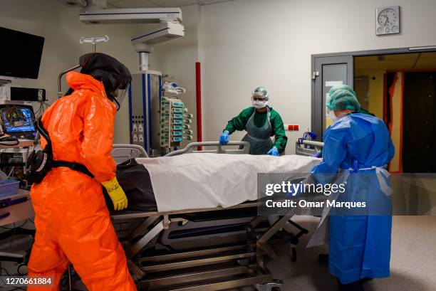 Medical personnel wear protective suits, masks, gloves and face shields as they transfer the body of a deceased COVID-19 patient to a metal coffin at...