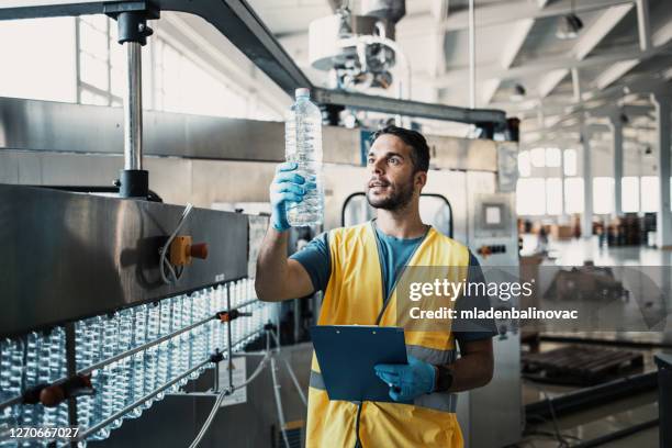 mannelijke arbeider in het bottelen fabriek die waterflessen controleert vóór verzending. inspectie kwaliteitscontrole. - bottle factory stockfoto's en -beelden
