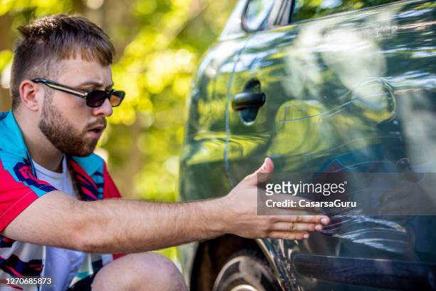 hombre adulto joven enojado apuntando a la puerta del coche rayado - abollado fotografías e imágenes de stock