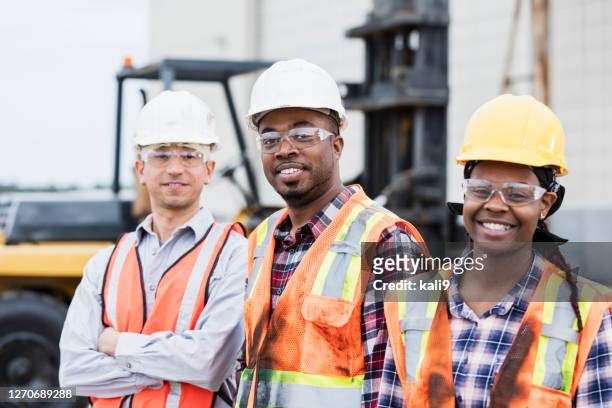trois ouvriers de construction dans des casques durs et des gilets de sécurité - ouvrier du bâtiment photos et images de collection
