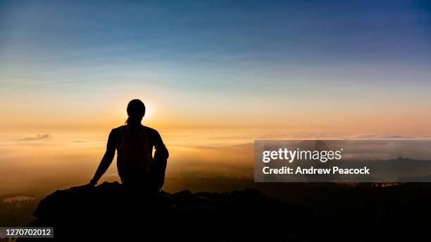 silhouette of a woman exploring sunrise sitting on boulder - watching sunrise stock pictures, royalty-free photos & images