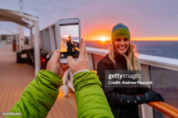 woman being photographed on smartphone while standing on deck of ship at sunset - antarctica people stock pictures, royalty-free photos & images