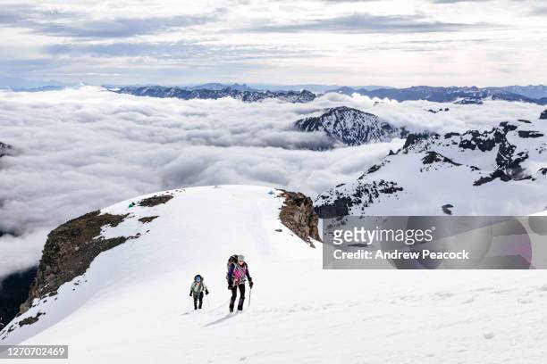 two mountain climbers ascending snowy slope, mount rainier national park, washington state, usa - mt rainier national park stock pictures, royalty-free photos & images