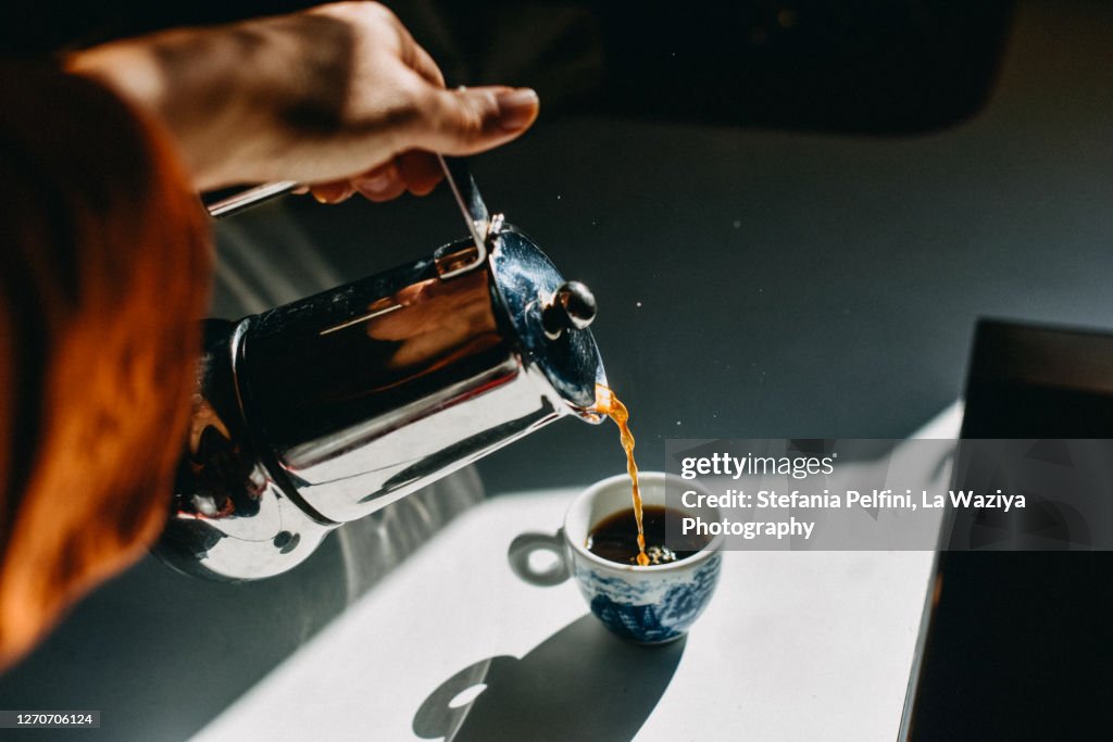 Pouring espresso coffee into an espresso cup with a mocha pot.