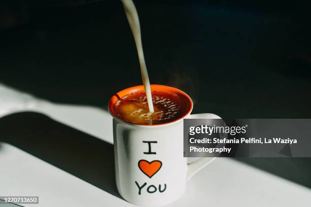 milk poured into a white mug filled with hot tea. - love you stockfoto's en -beelden