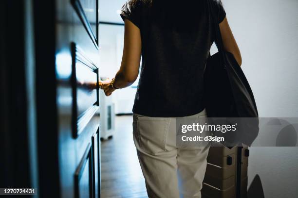 rear view of young asian female traveller opening the door entering the hotel room. she is carrying a suitcase and on vacation - apartment entry stock pictures, royalty-free photos & images