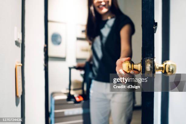 cheerful young asian female traveller opening the door entering the hotel room. she is carrying a suitcase and on vacation - entrée appartement photos et images de collection