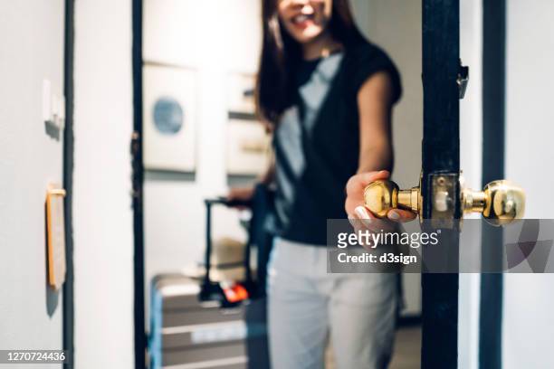 cheerful young asian female traveller opening the door entering the hotel room. she is carrying a suitcase and on vacation - arrival stock pictures, royalty-free photos & images