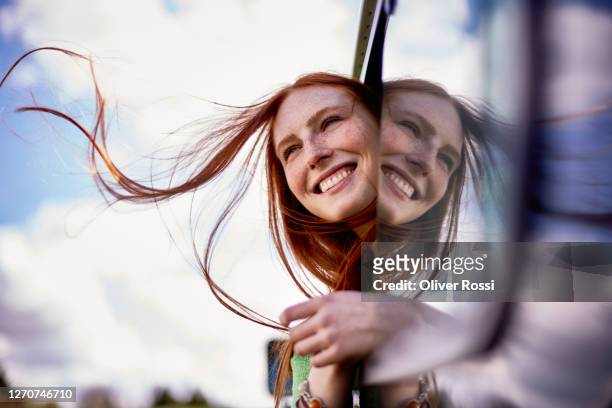happy redheaded young woman leaning out of car window - freude stock-fotos und bilder