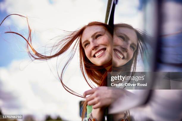 happy redheaded young woman leaning out of car window - visage caché par les cheveux photos et images de collection