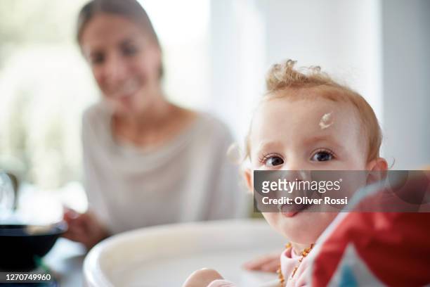 portrait of baby girl with food remains in her face and mother in background - cute food stock pictures, royalty-free photos & images