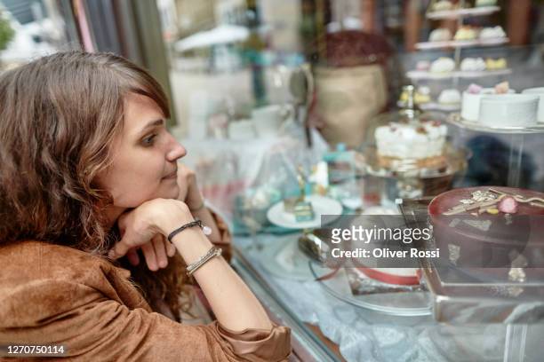 young woman looking in shop window of a confectioner - temptation stock pictures, royalty-free photos & images
