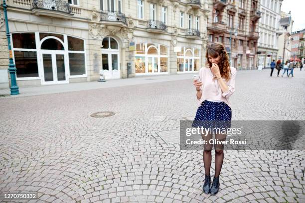 smiling young woman in the city looking at cell phone - zone piétonnière photos et images de collection