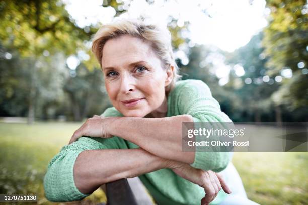 portrait of confident mature woman sitting on a park bench - mujer 50 años fotografías e imágenes de stock