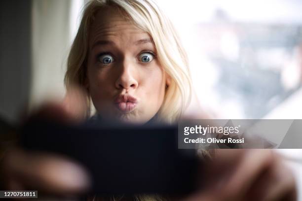playful young woman grimacing while taking a selfie - gesicht verziehen stock-fotos und bilder