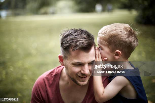 son whispering into father's ear - flüstern stock-fotos und bilder
